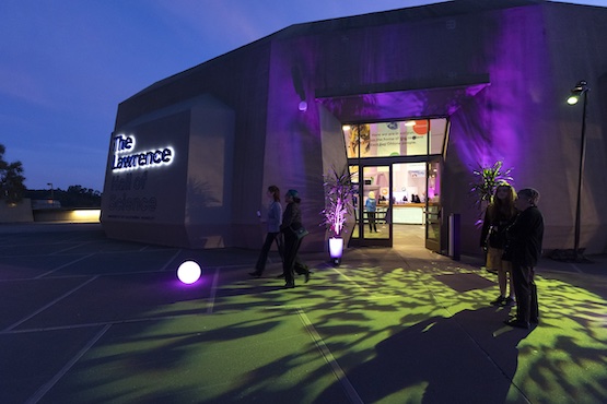 A view of the Lawrence Hall of Science from the plaza at dusk. The front door is illuminated in purple. 