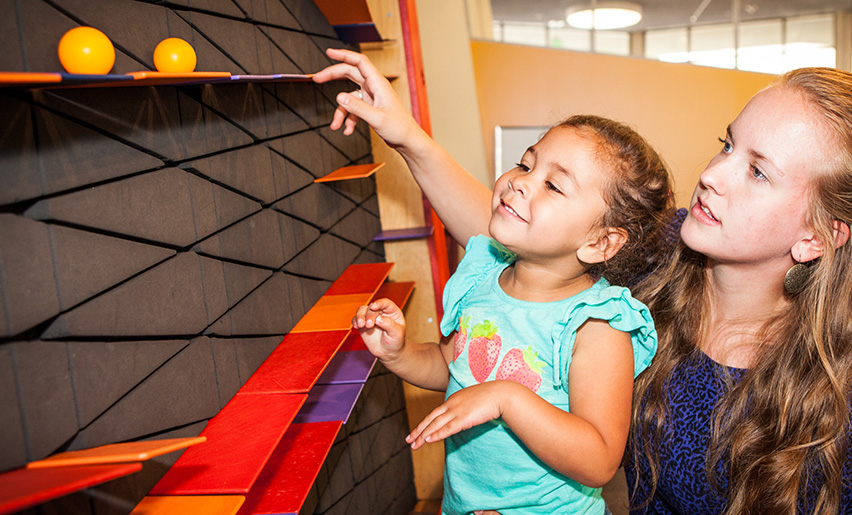 A child and an adult reach for a ball at a science exhibit