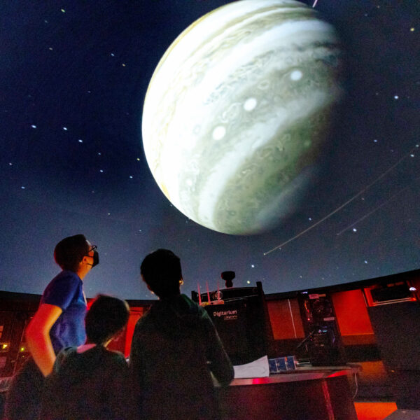 Inside view of the Planetarium with Lawrence staff and visitors. A large planet is shown on the dome.