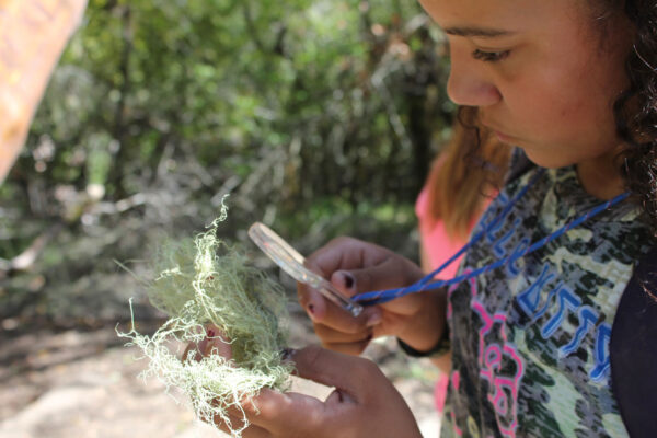 A student is outdoors examining nature through a magnifying glass
