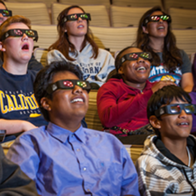 People are watching a science film in the 3D theater wearing 3D glasses