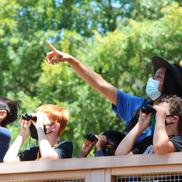 A teen volunteer and young students are making observations of nature in the Outdoor Nature Lab.